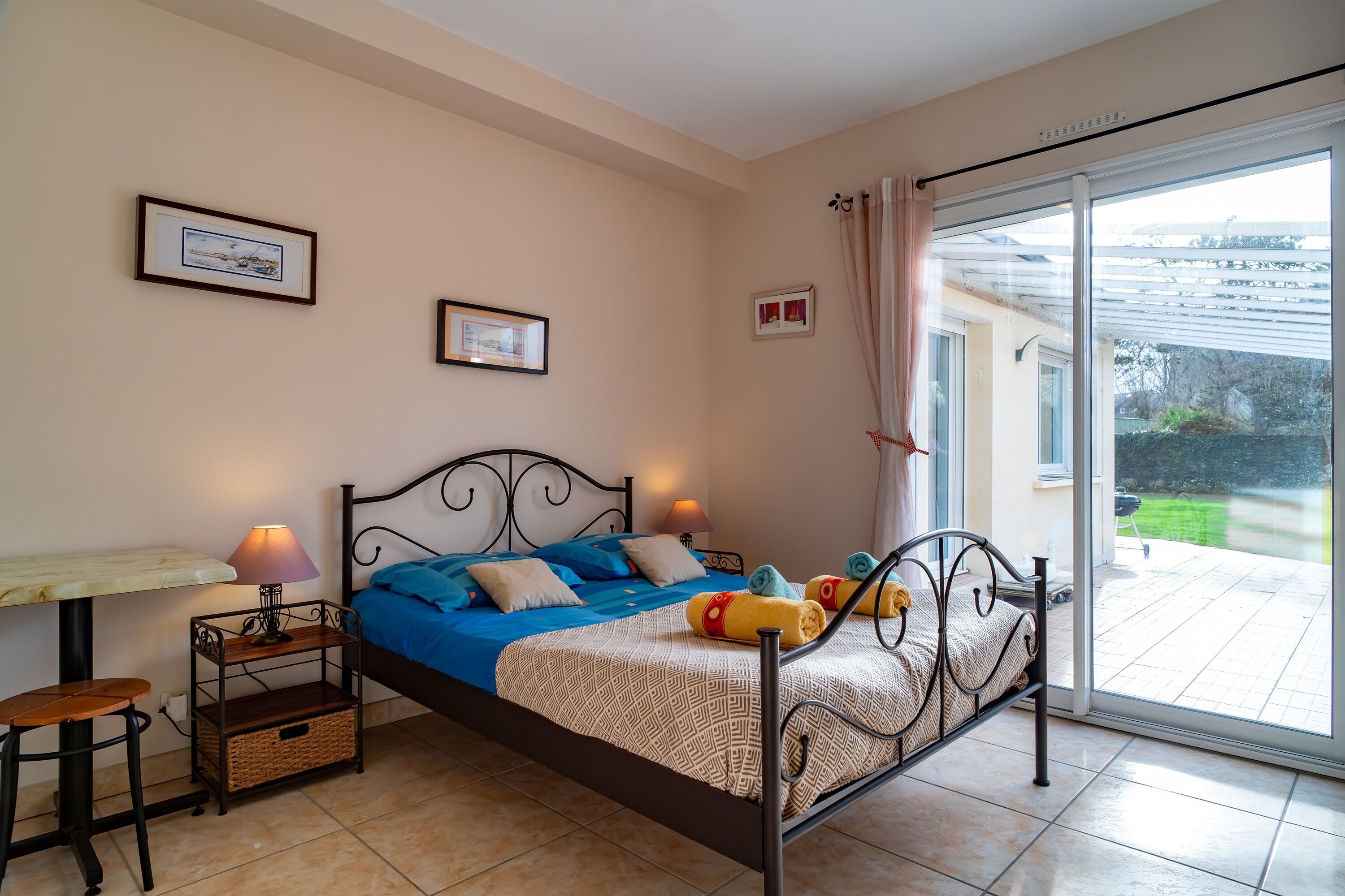 Un dormitorio con una cama, una mesa y una silla. Hay cuadros en la pared y una ventana con cortinas.