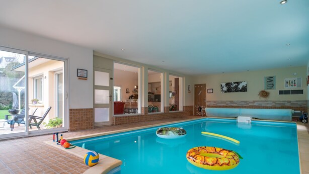 En indendørs swimmingpool med glasdøre, der fører til en terrasse.