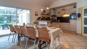 Et rummeligt køkken med moderne hårde hvidevarer, et spiseområde med fletstole og en stor skydedør, der fører ud til en terrasse.