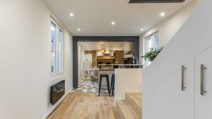 A modern kitchen with a central island, wooden flooring, and a view into the dining area. - Aux Magnolias - Maison pour 6p (Silly-Tillard)