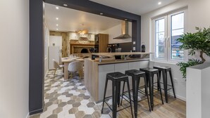 A modern kitchen with a central island, bar stools, and a view of the dining area. - Aux Magnolias - Maison pour 6p (Silly-Tillard)