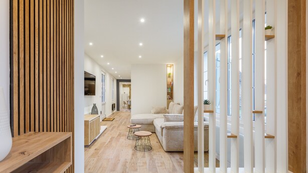 A modern living room with a sofa, coffee table, and a TV. There is a wooden floor and a white wall with a wooden panel. - Aux Magnolias - Maison pour 6p (Silly-Tillard)