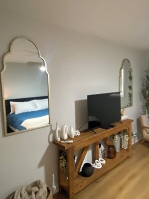 Ein Hotelzimmer mit einem Bett, einem Fernseher auf einer Holzkonsole, dekorativen Vasen und einem Spiegel an der Wand.
