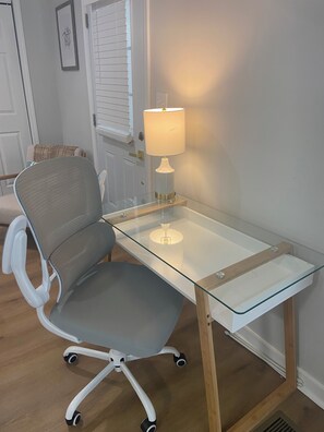 Ein moderner Bürostuhl auf Rädern, ein Glastisch und eine Wandleuchte.