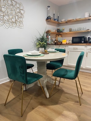 Ein Essbereich mit einem runden Tisch, vier Türkis-Stühlen und einem Blumentopf.