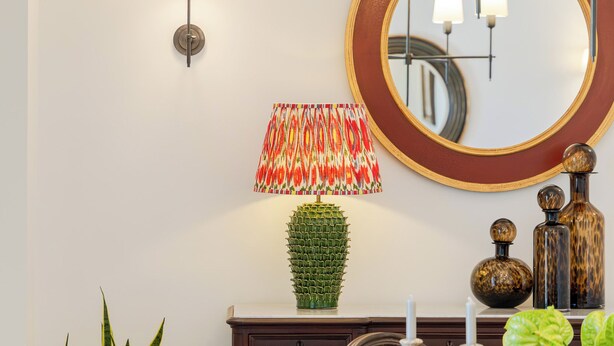 En spiseplads med et rundt bord, stole, en potteplante, en dekorativ lampe og væglamper.