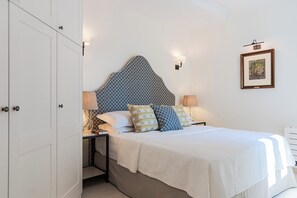 Ein ordentlich bezogenes Bett mit gemusterten Kissen, einer Nachttischlampe und einem gerahmten Bild an der Wand.