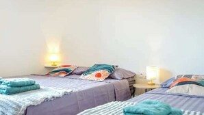 A hotel room with two beds, each with a patterned bedspread and pillows, a bedside table with a lamp, and a wall-mounted light.