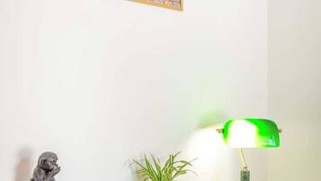 Une pièce avec une lampe de bureau verte, une petite plante en pot et un tableau encadré accroché au mur.