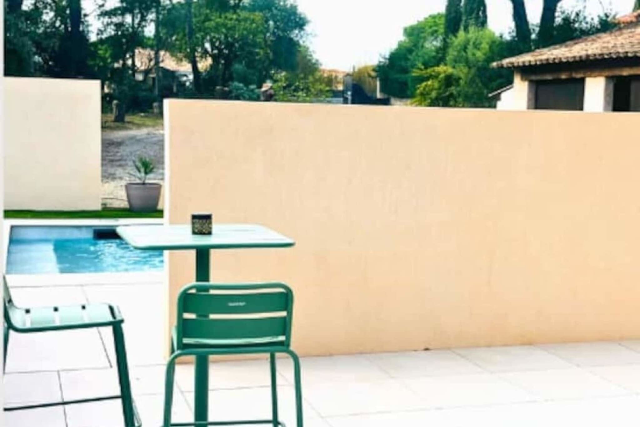 A poolside area with a table and two chairs, a potted plant, and a beige wall.