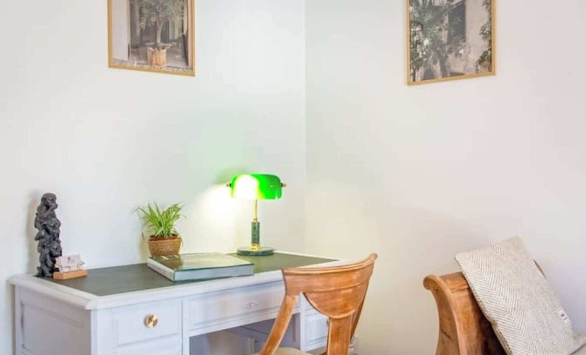 A desk with a lamp, a chair, a small statue, and two framed pictures on the wall.