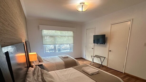 Habitación de hotel con dos camas, televisión, ventana y puerta.
