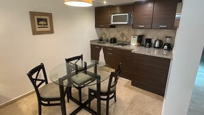 Una cocina compacta con armarios de madera oscura, un microondas y una mesa de vidrio con cuatro sillas.