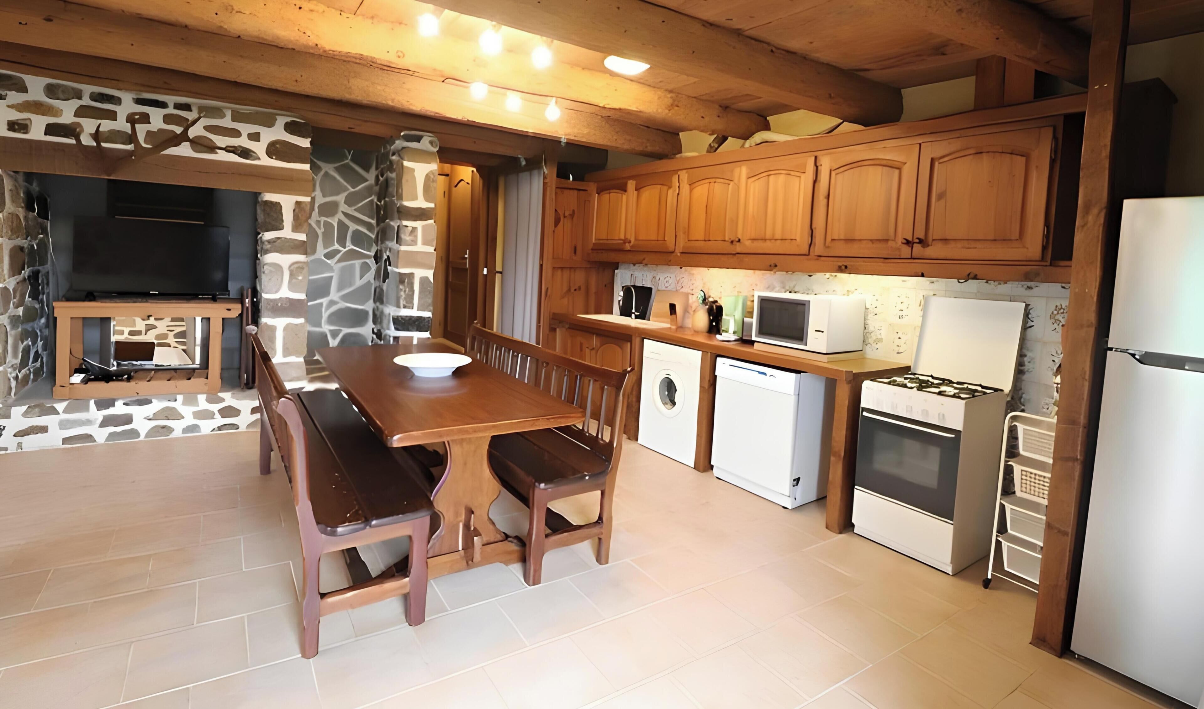 A kitchen with wooden cabinets, a stone wall, a dining table with chairs, and a built-in oven.