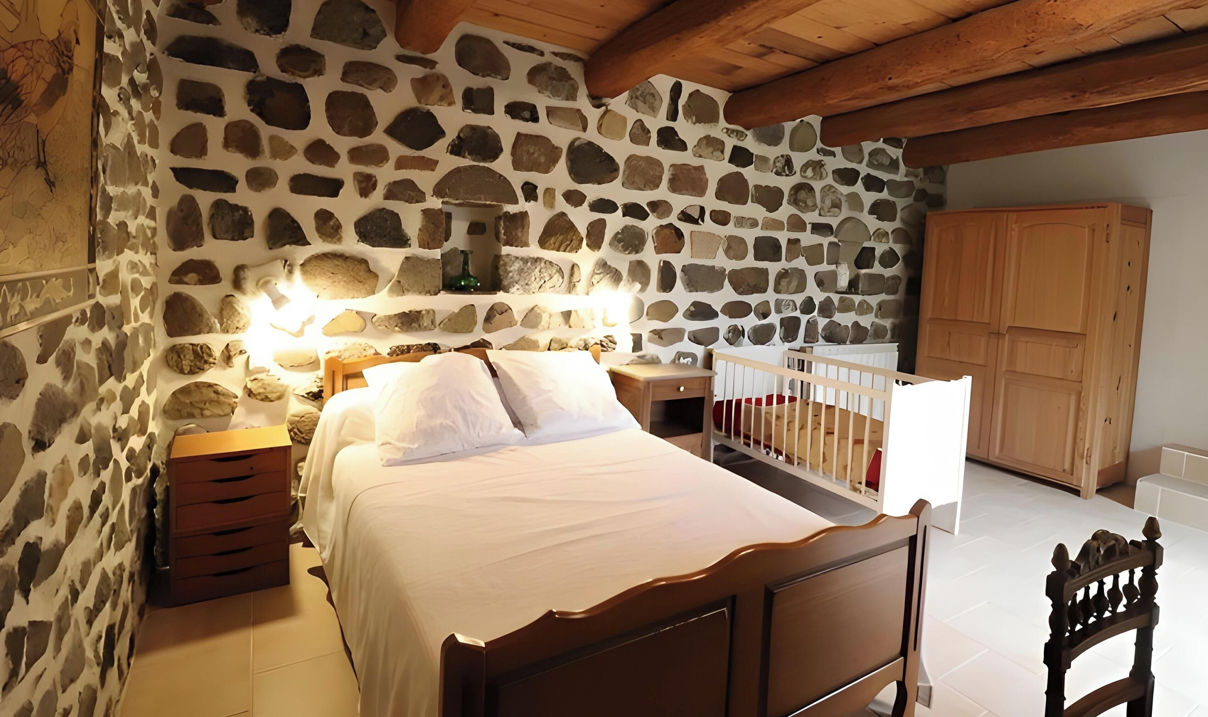 A bedroom with a stone wall, wooden bed frame, bedside tables, and a wooden wardrobe.