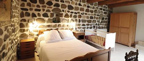 A bedroom with a stone wall, wooden bed frame, bedside tables, and a wooden wardrobe.