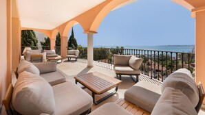 A covered outdoor seating area with sofas and a table, overlooking a coastal view.