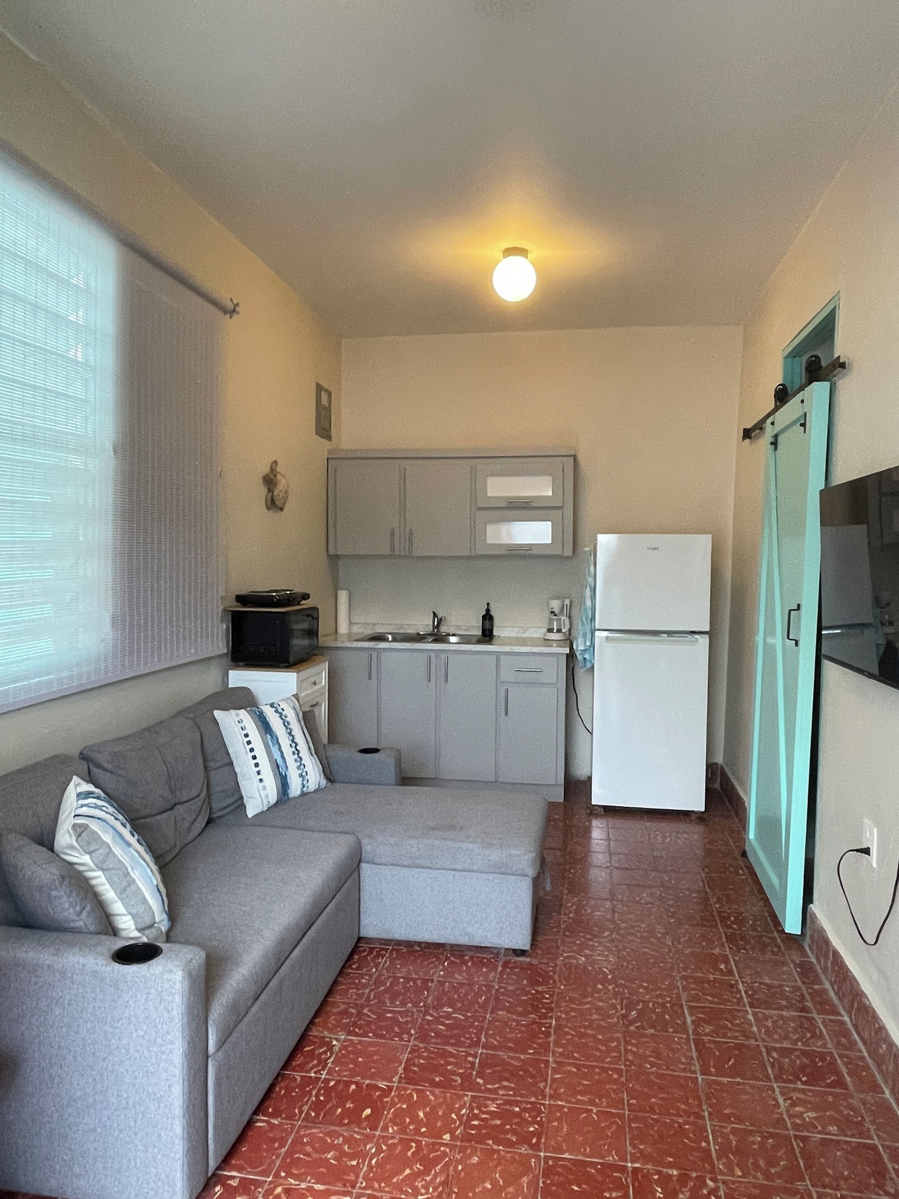 A compact kitchen with a grey sofa, a small refrigerator, and a tiled floor.