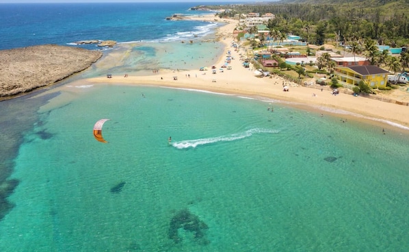 Un complexe hôtelier de bord de mer doté d’eaux turquoise et limpides, d’une plage de sable et de plusieurs bâtiments intégrés dans un cadre tropical.
