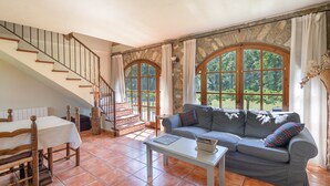 A living room with a staircase, a sofa, a dining table, and large windows.