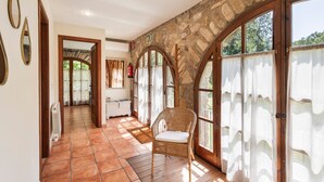A corridor with a wicker chair, stone walls, and large windows with curtains.