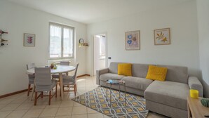 A living room with a grey sofa, yellow pillows, a dining table with chairs, and a patterned rug. - Apartment in the center of Bergamo and at the foot of the city high with private parking (Bergamo)