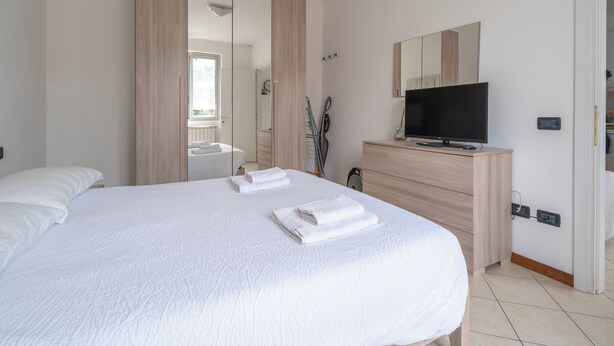 A bedroom with a bed, a TV on a dresser, a mirror, and a sliding door leading to a bathroom. - Apartment in the center of Bergamo and at the foot of the city high with private parking (Bergamo)