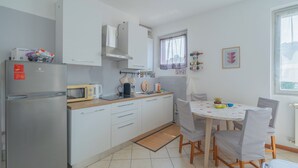 A compact kitchen with a refrigerator, microwave, and stove, a dining area with a table and chairs, and a window with curtains. - Apartment in the center of Bergamo and at the foot of the city high with private parking (Bergamo)
