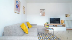 A modern living room with a grey sofa, yellow cushions, a patterned rug, a flat-screen TV, and a small table with books and a plant. - Apartment in the center of Bergamo and at the foot of the city high with private parking (Bergamo)