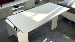 Moderni olohuone, jossa on valkoinen sohva, valkoinen sohvapöytä ja televisio, jolta näkyy piirrettyjä.