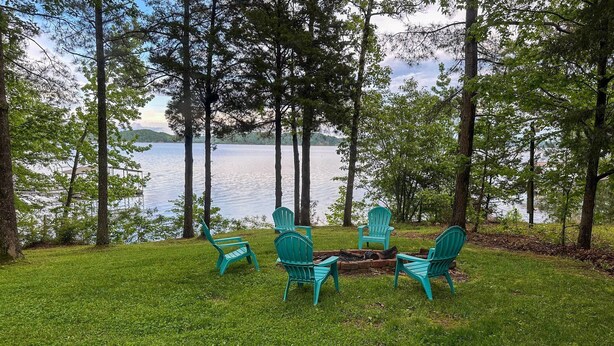 Area salotto sul lago con quattro poltrone Adirondack color turchese disposte attorno a un braciere.