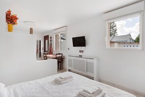 Een slaapkamer met een bed, een televisie, een raam en een bureau met een stoel.