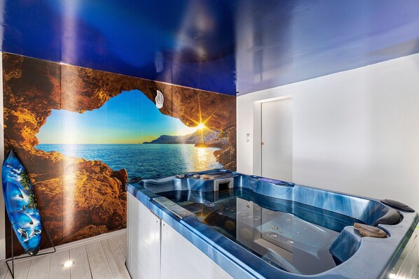 Ein Wellnessbereich mit Whirlpool, einem Wandgemälde mit Sonnenuntergang über dem Meer und einem Surfbrett.
