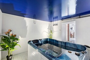 Ein modernes Badezimmer mit einer Glaskonstruktion für eine Whirlwanne, einem Blumentopf und einem Spiegel, der den Raum reflektiert.