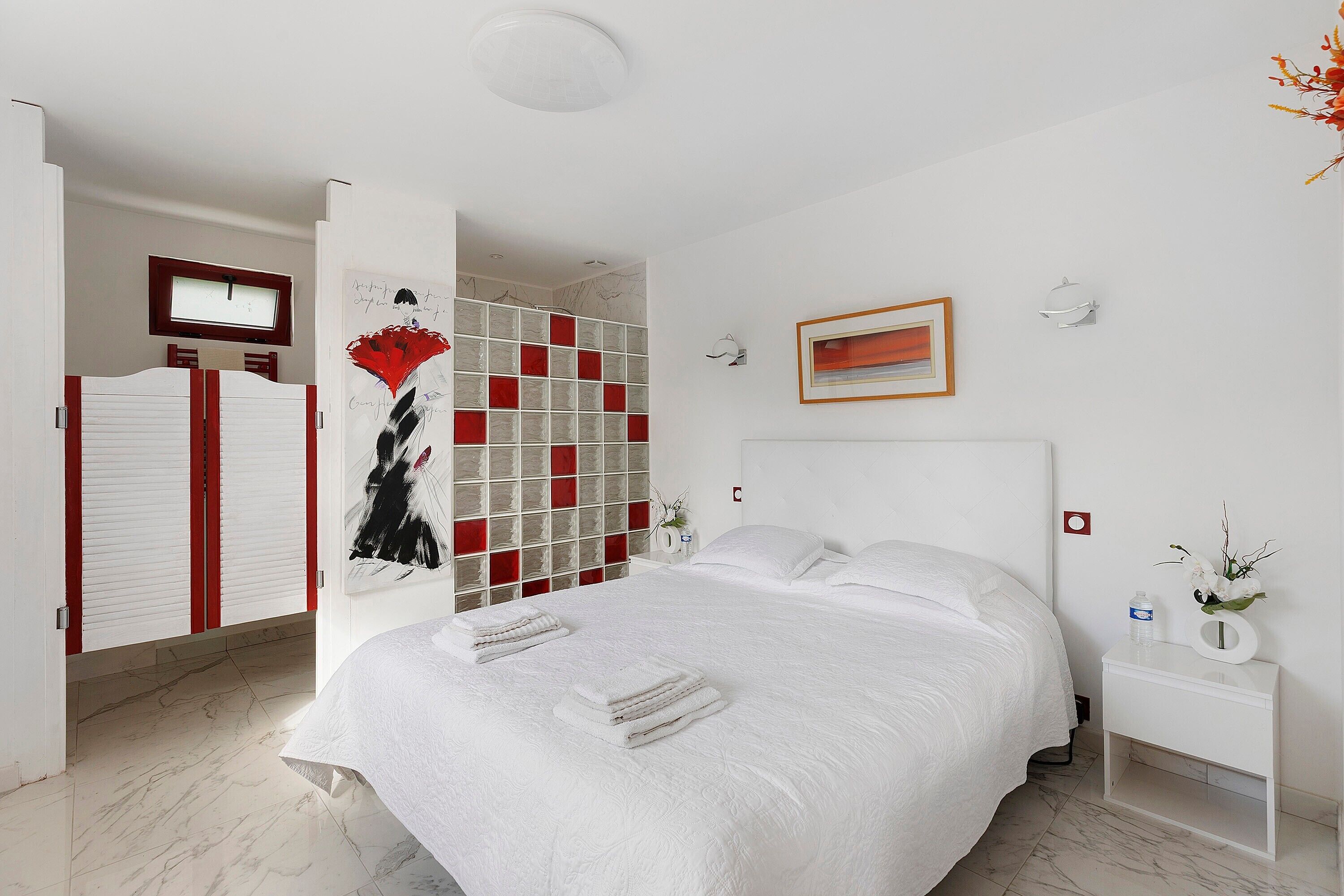 Hotelkamer met een groot bed, nachtkastje, kledingkast en een wand met een rood-wit patroon.