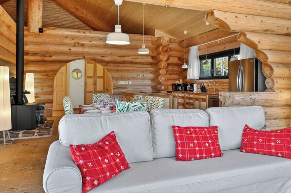 A log cabin interior with a sofa, kitchen, and dining area. - Cedar Heaven Lake Lodge (Guysborough)