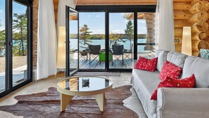 Un intérieur moderne avec un canapé en cuir, une table basse en verre et une vue sur un lac et des arbres, visible à travers de grandes portes vitrées.
