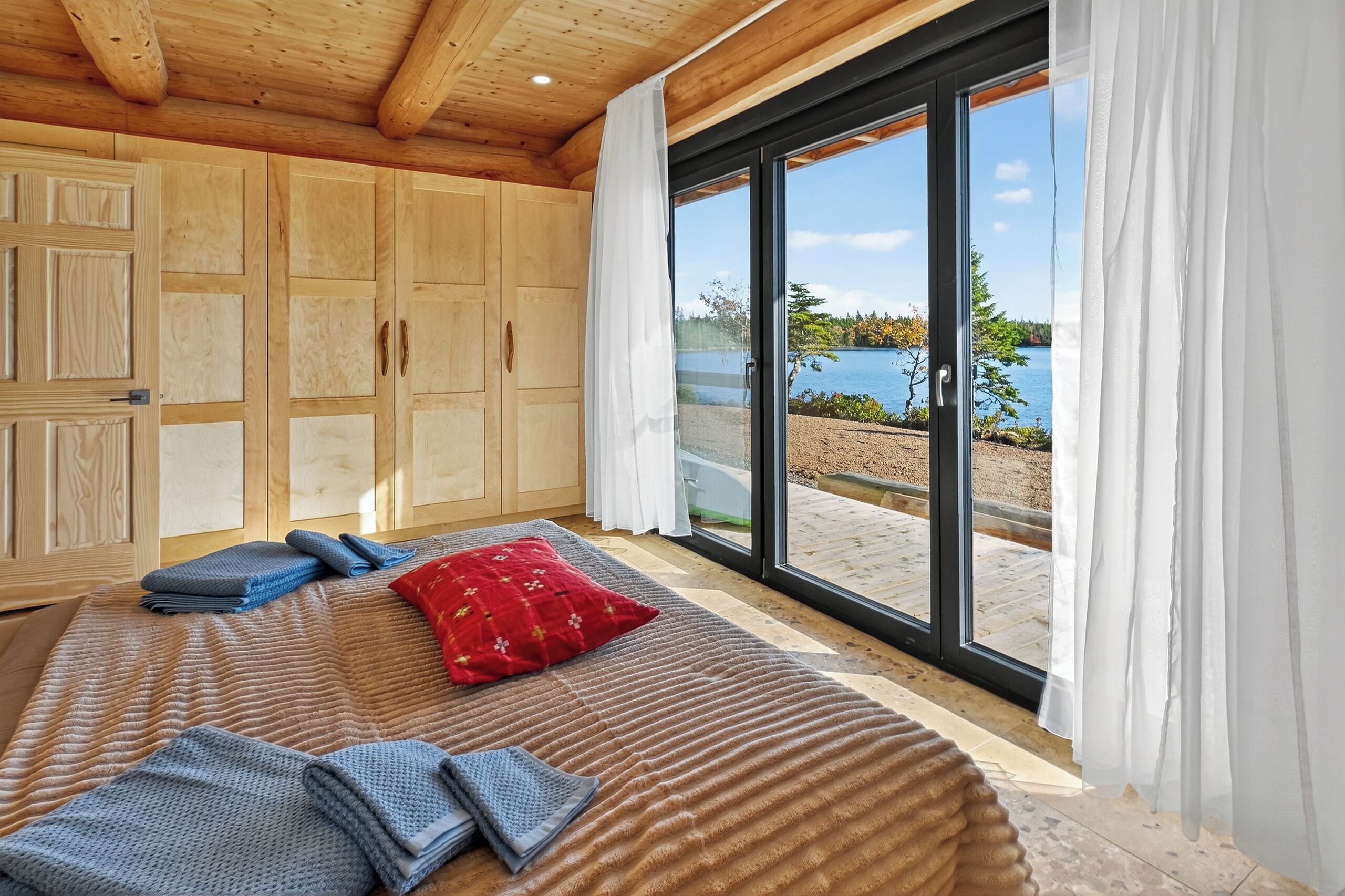 Une chambre avec un grand lit, une armoire en bois et une vue sur un lac, visible à travers une porte-fenêtre coulissante.