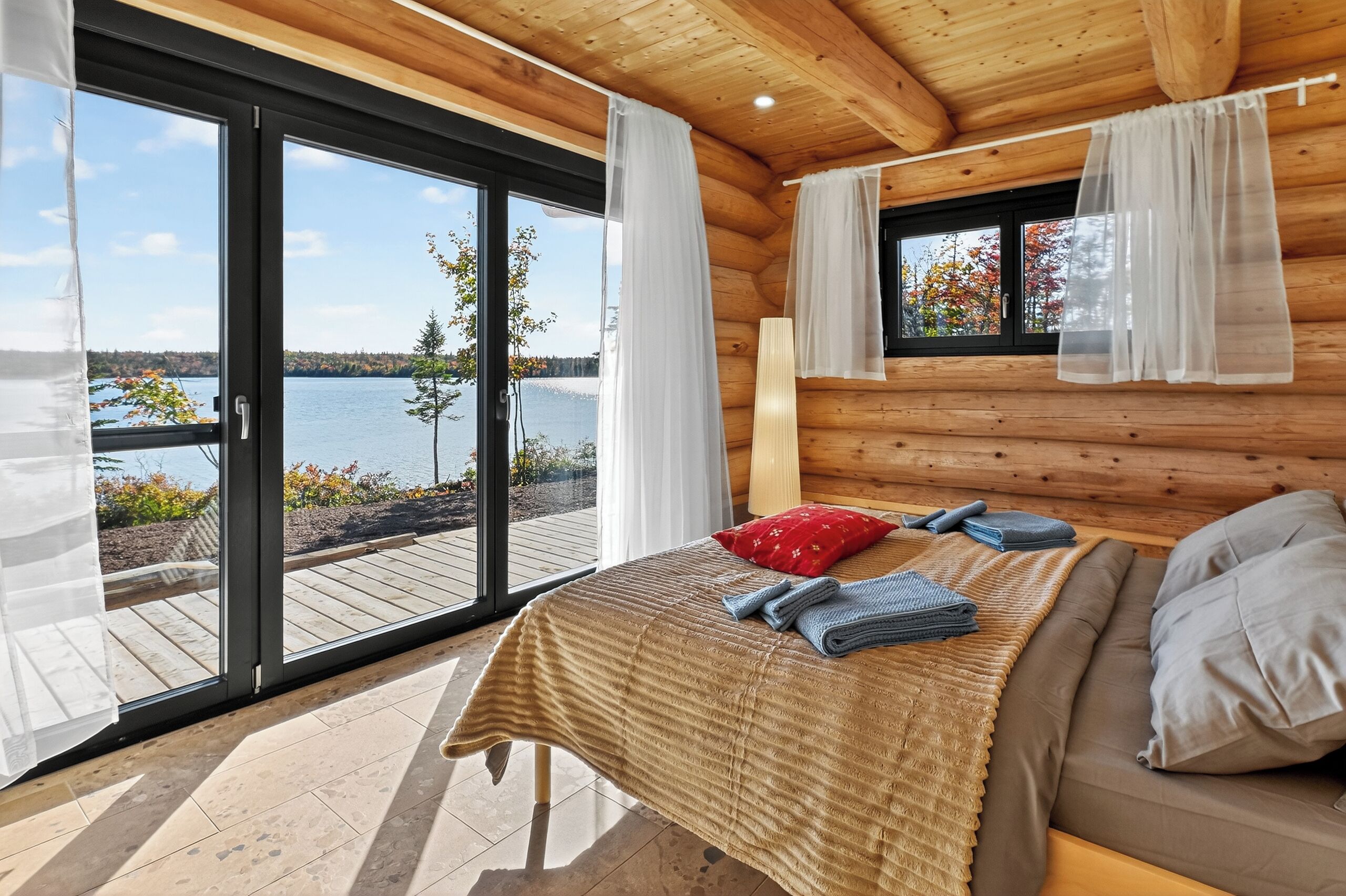 A wooden cabin bedroom with a bed, pillows, and a view of a lake.