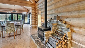 L’intérieur d’une cabane en rondins comprend un coin repas, une cheminée en pierre et de grandes fenêtres.