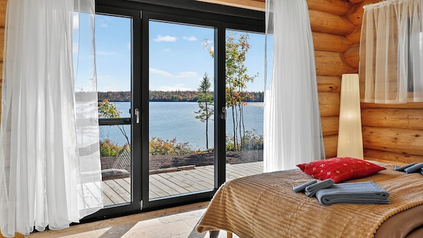 Une chambre dotée d’une grande porte-fenêtre coulissante donnant sur une terrasse avec vue sur un lac.