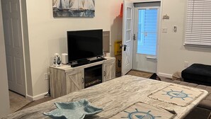 Un coin repas avec une longue table, des chaises, un téléviseur et un tableau représentant un voilier accroché au mur.