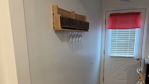 Un couloir avec une étagère en bois où sont posés des verres à vin, une porte ornée d’une lambrequin rouge et un plancher en bois.
