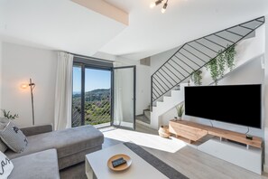 A modern living room with a sofa, a coffee table, a TV, a staircase, and a balcony with a view.