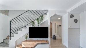 A modern living room with a staircase, a flat-screen TV, and a wooden coffee table.
