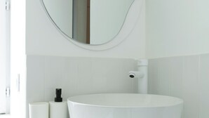 Ein modernes Badezimmer mit rundem Spiegel, weißem Waschbecken und weißen Fliesen.