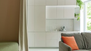 Ein modernes Wohnzimmer mit einem grauen Sofa, einem grünen Sitzsofa und einem weißen Küchenbereich mit einem Fenster.