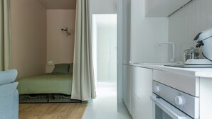 Eine kompakte Küche mit weißen Geräten, ein Bett mit grüner Bettwäsche und ein Holzboden.