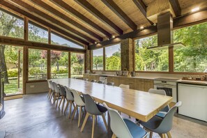 A spacious kitchen with large windows, a long wooden table, and modern chairs.