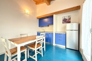 Eine kleine Küche mit Holztisch und -stühlen, blauen Schränken und einem weißen Kühlschrank.
